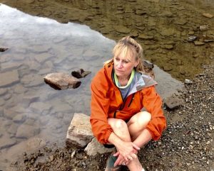 Marlo Bennett wearing an orange jacket, sitting at a lake's edge