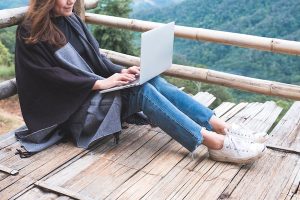 closeup of woman working on laptop on wooden balcony against green mountain background