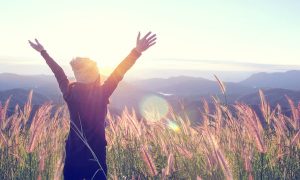 happy woman atop mountain meadow enjoying sunrise