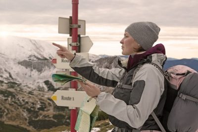 Female hiker in warm clothes at trail sign referencing map