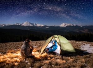 couple winter camping under night stars and snow mountains in background